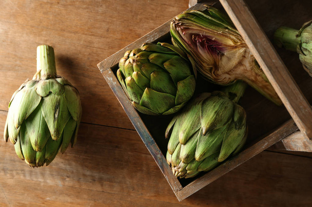 Basket with raw artichokes on wooden table - Photo, Image