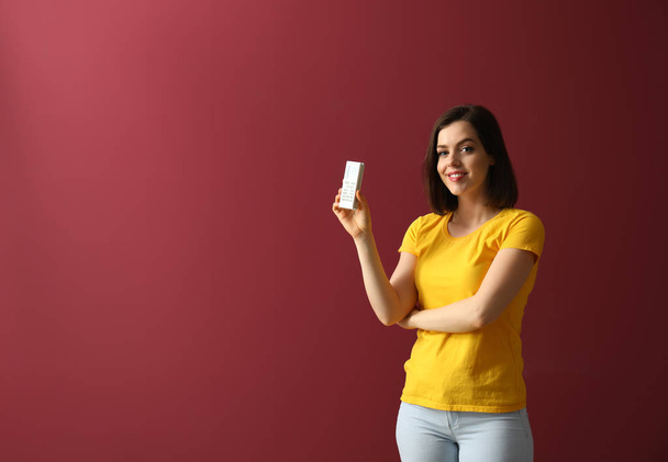 Young woman with air conditioner remote control on color background - Foto, Bild