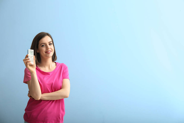 Junge Frau mit Klimaanlage-Fernbedienung auf hellem Hintergrund - Foto, Bild