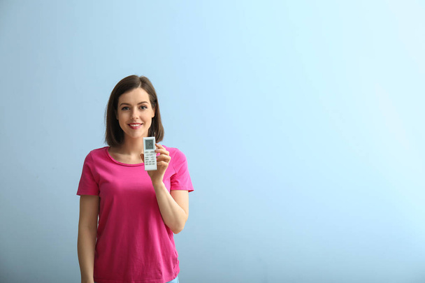 Young woman with air conditioner remote control on light background - Photo, Image