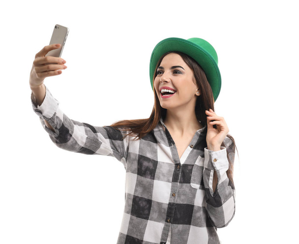 Beautiful young woman in green hat taking selfie on white background. St. Patrick's Day celebration - Photo, Image