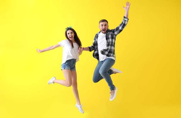 Jumping young couple on color background - Foto, afbeelding