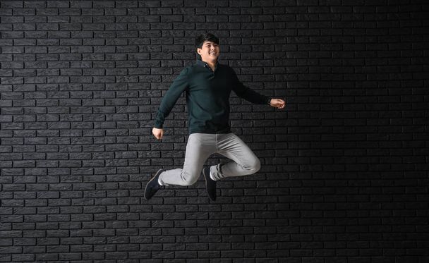 Saltando homem asiático contra fundo de tijolo escuro
 - Foto, Imagem