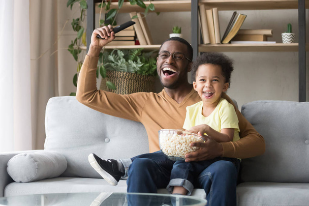 Excited black father with toddler son watching sport tv game - Foto, Bild
