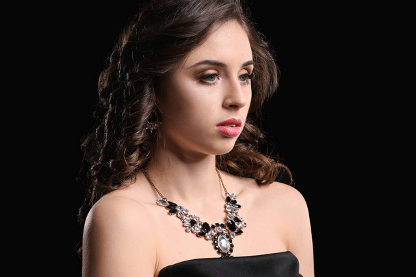 Young woman with beautiful jewelry on dark background - Фото, изображение