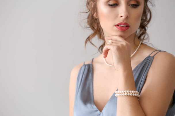 Young woman with beautiful pearl jewelry on light background - Photo, Image
