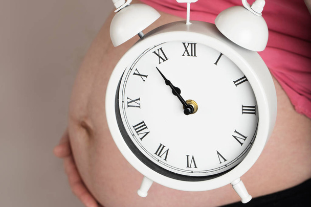 Mujer embarazada joven mantiene reloj despertador vintage cerca de su campana
 - Foto, imagen