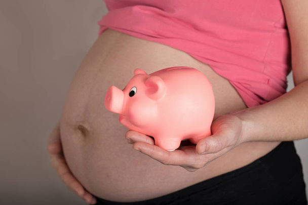 Молодая беременная женщина держит розовую копилку
.  - Фото, изображение