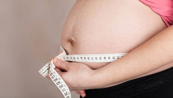 Молодая беременная женщина измеряет свой живот с помощью измерительной ленты
.  - Фото, изображение