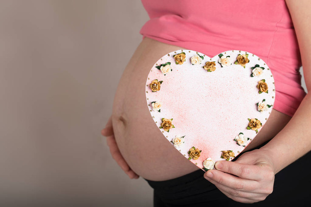 Fiatal terhes nő tartja díszített papír szív  - Fotó, kép