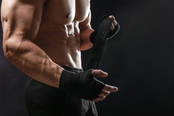 Attractive sportsman winding wrist band against dark background - Фото, изображение