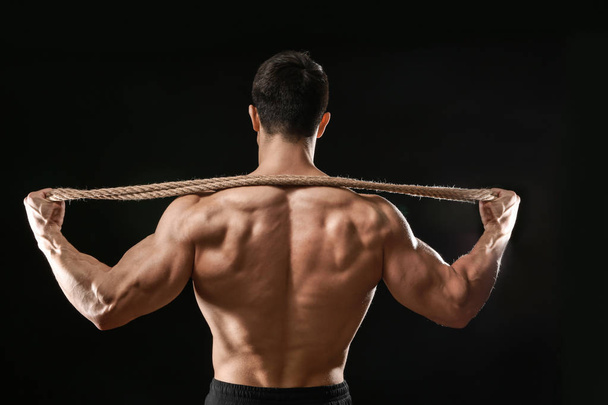Muscular bodybuilder with rope on dark background, back view - Zdjęcie, obraz