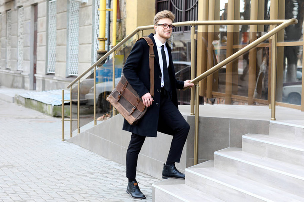 Handsome businessman with stylish briefcase going upstairs outdoors - 写真・画像