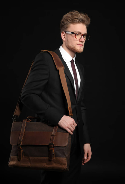 Handsome businessman with stylish briefcase on dark background - Фото, изображение