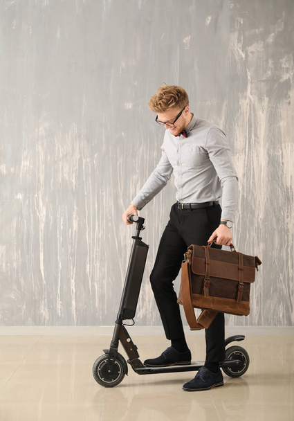Handsome businessman with stylish briefcase and scooter near grey wall - Foto, immagini