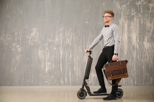 Bello uomo d'affari con valigetta elegante e scooter vicino alla parete grigia
 - Foto, immagini