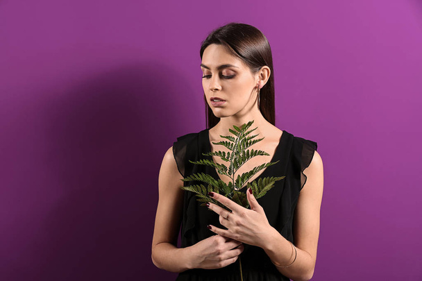 Young woman with beautiful jewelry and tropical leaf on color background - Photo, Image