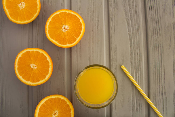Orange juice in the glass  and halves of oranges on the grey wooden background.Top view.Copy space. - Foto, Imagem
