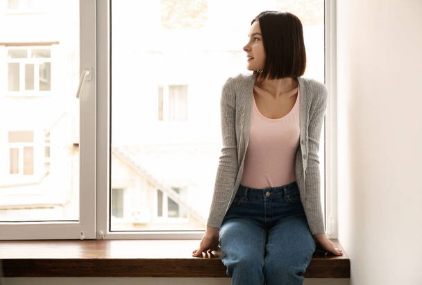 Young woman sitting on window sill at home - Фото, зображення