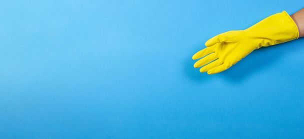 Una mano de mujer en guante de goma amarillo sobre fondo azul
 - Foto, imagen