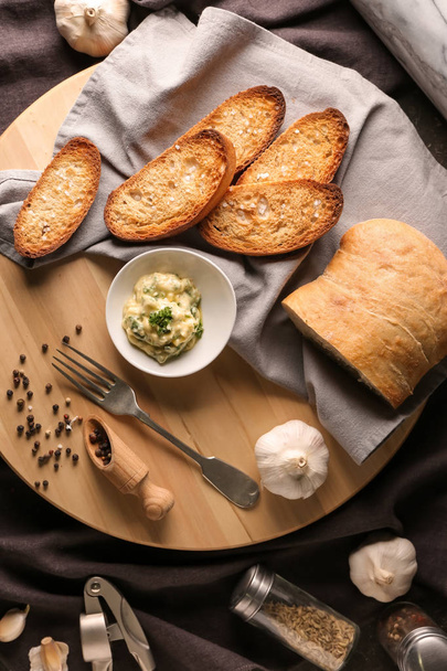 Sliced bread and garlic spreading on wooden board - Фото, изображение