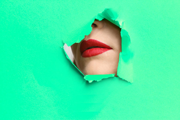 Beautiful woman with bright makeup visible through hole in color paper - Fotó, kép