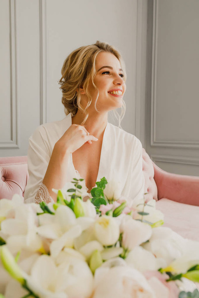 young beautiful wedding bride is sitting on a pink bed in a bright room and smiling - Foto, afbeelding