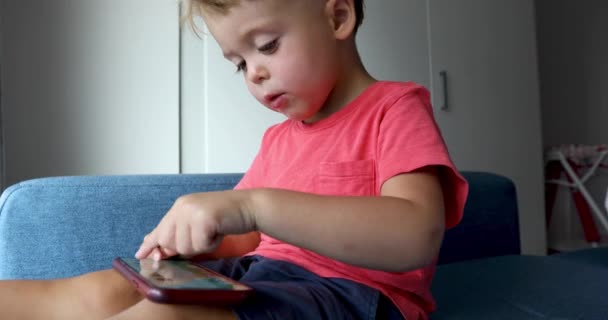 Content kid playing smartphone on sofa - Záběry, video