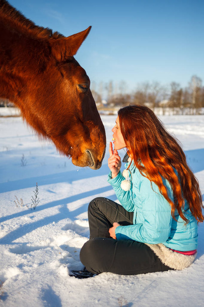 Red-haired girl in a snowy field feeds an apple from hands - Fotografie, Obrázek