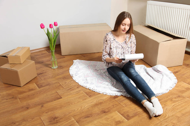 girl sitting on wooden floor near boxes in new apartment - Photo, Image