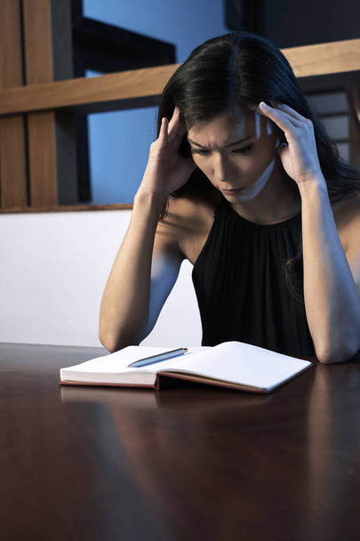 Depressieve jonge vrouw kijken naar lege pagina in haar dagboek en haar problemen na te denken - Foto, afbeelding