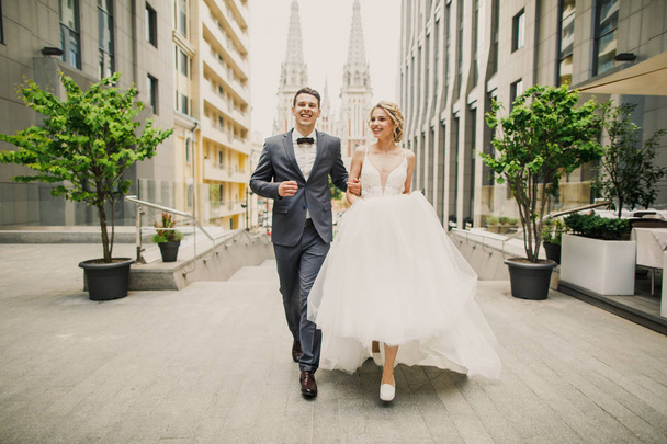 young beautiful couple bride and groom walk in the city on the background of the church and smile the bride in a beautiful dress the groom dressed stylishly - Zdjęcie, obraz