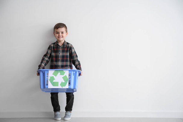 Niño pequeño con canasta de basura cerca de la pared blanca. Concepto de reciclaje
 - Foto, imagen