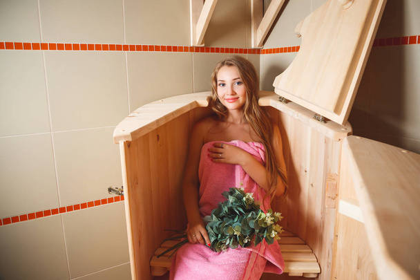 The beautiful girl sits in an open cedar barrel with a broom from birch branches. National Russian rest in baths - Foto, Imagem