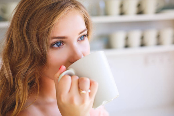 The nice girl in kitchen drinks from a mug in the morning - Photo, image