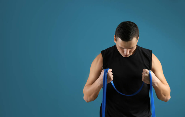 Sporty young man training with resistance band against color background - Fotografie, Obrázek