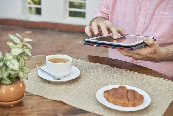 Close-up beeld van de mens bezig met tablet pc en ontbijten op terras - Foto, afbeelding