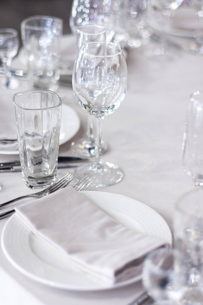 Wine glasses are on the table on a white tablecloth.  The table is set for the holiday. White napkins on the plates - Φωτογραφία, εικόνα