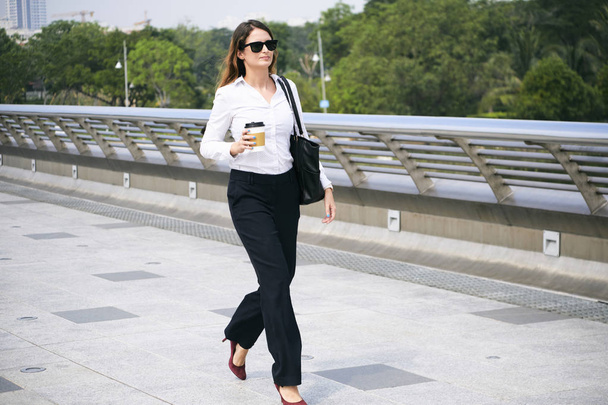 Élégante dame d'affaires marchant avec une tasse de café jetable dans les mains
 - Photo, image