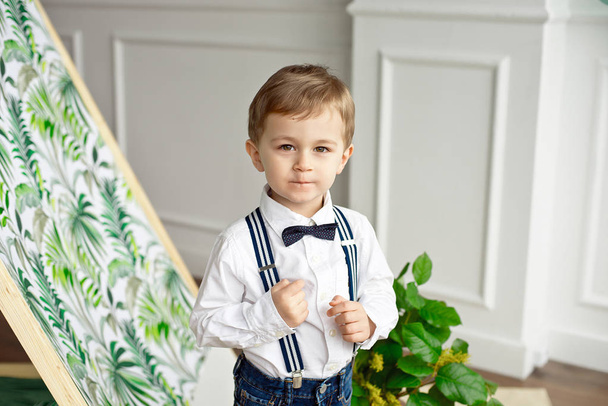 Cute boy in a white shirt and bow tie stands in a room near the tent with a smile. - 写真・画像