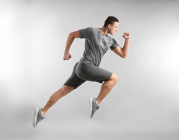 Σπορ νεαρός άνδρας τρέχει εναντίον γκρι φόντο - Φωτογραφία, εικόνα