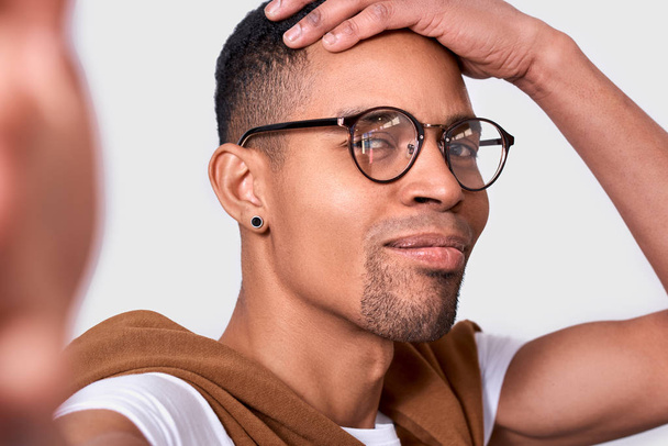 Closeup image of happy handsome African American young man smiling, wearing eyewear, looking at the camera and taking self portrait. Cheerful male posing in studio background. People and emotion - Foto, immagini