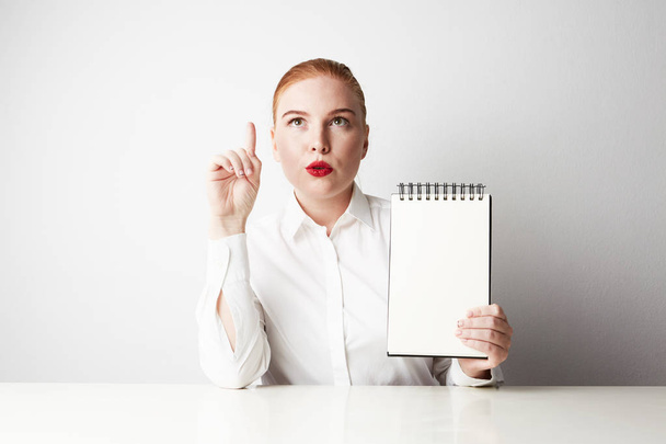 Pelirroja mujer de negocios posando en camisa sosteniendo bloc de notas vacío sobre fondo blanco
. - Foto, Imagen