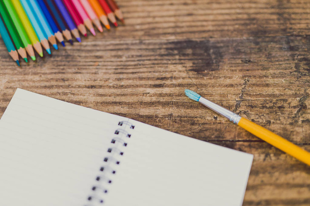 notebook with brushes and color pencils on wooden desk - Fotografie, Obrázek