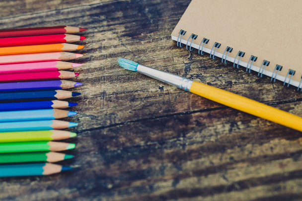notebook with brushes and color pencils on wooden desk - 写真・画像