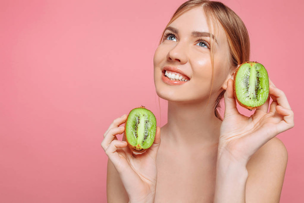 Attractive girl holding kiwi slices, on a pink background. Natur - Фото, изображение