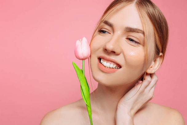 Beautiful young girl with clean skin, holding a pink flower near - Foto, afbeelding