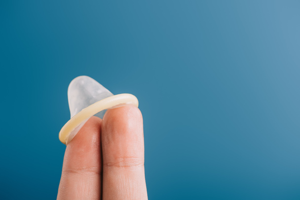 abgeschnittene Ansicht von zwei Fingern mit Kondom auf blauem Grund, Verhütungskonzept - Foto, Bild