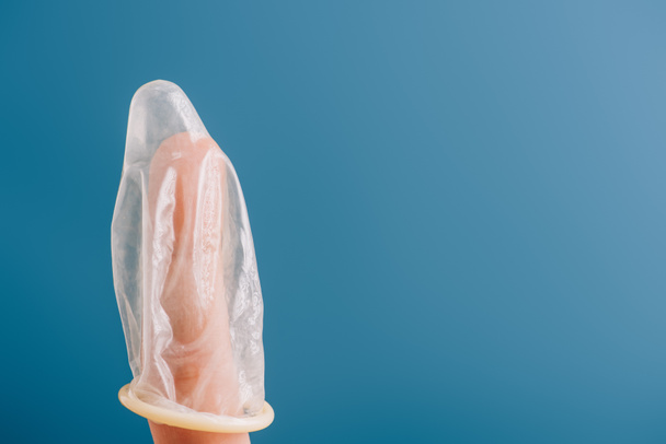 partial view of finger with condom isolated on blue, contraception concept - Photo, Image