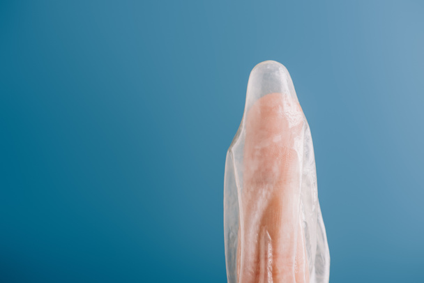 cropped view of finger with condom isolated on blue, contraception concept - Foto, Imagen